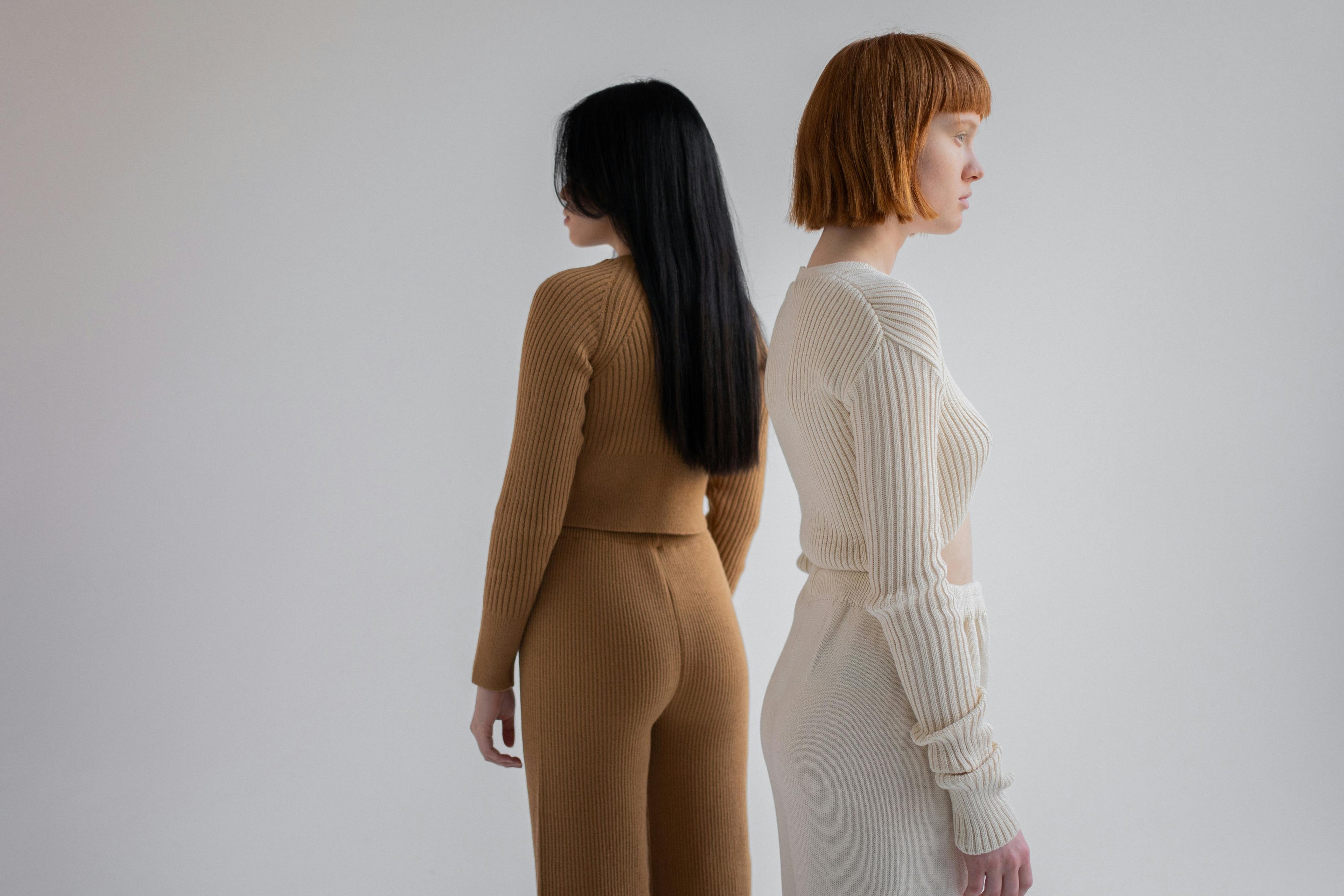 Two women standing back-to-back wearing matching ribbed knit outfits on a plain background